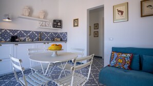 A compact kitchen with a white table and chairs, a blue patterned backsplash, and a teal sofa with colorful pillows. - Zisa Top Romantic terrace & private outdoor Jacuzzi (Palermo)