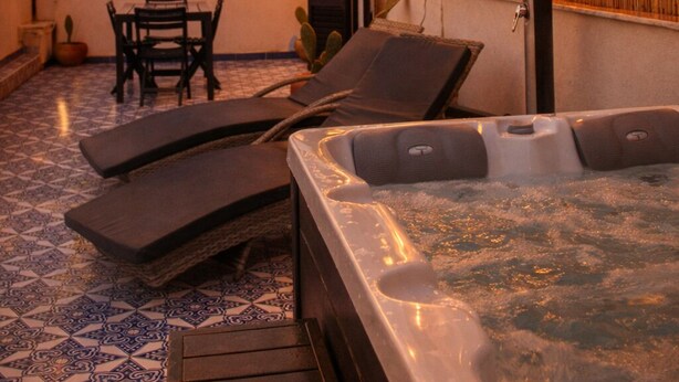 A rooftop patio with a hot tub, string lights, and a table with chairs. - Zisa Top Romantic terrace & private outdoor Jacuzzi (Palermo)