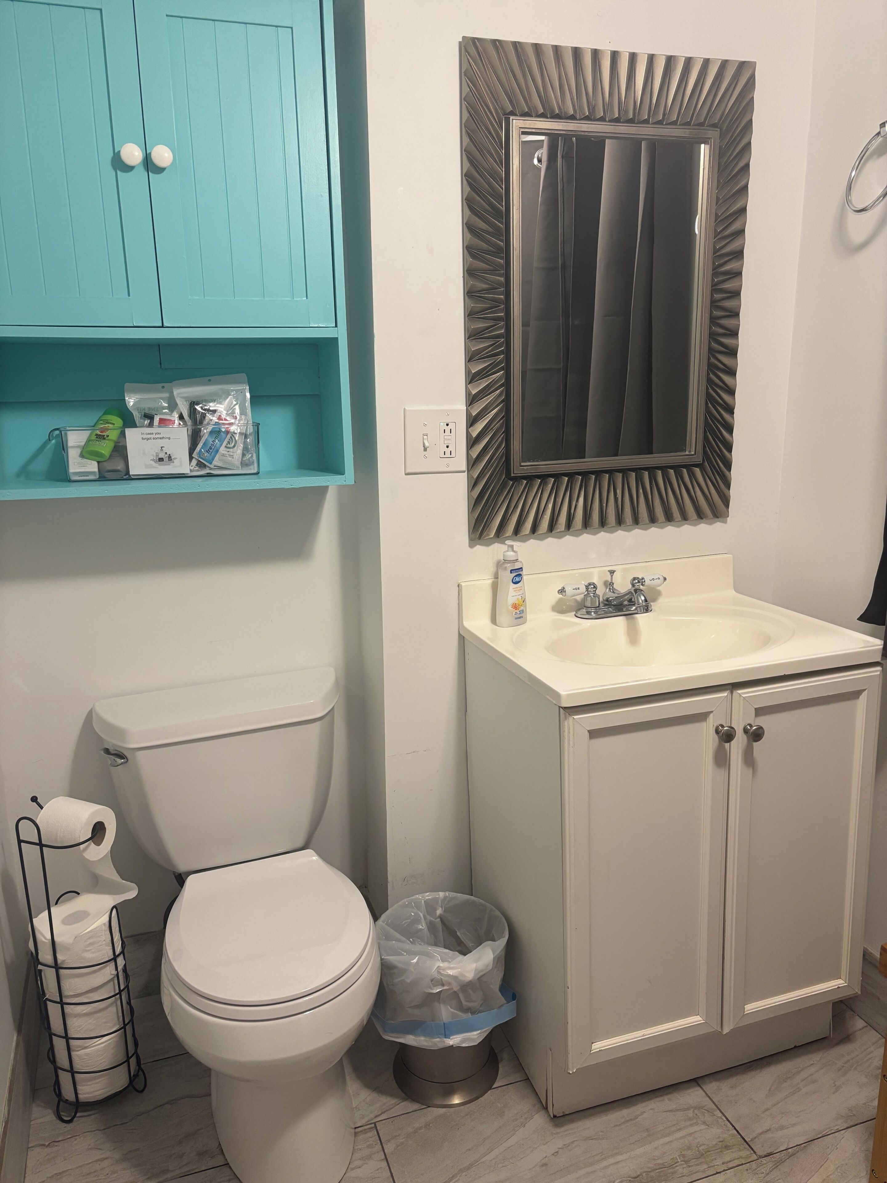 A bathroom with a toilet, sink, mirror, and a blue cabinet with toiletries.
