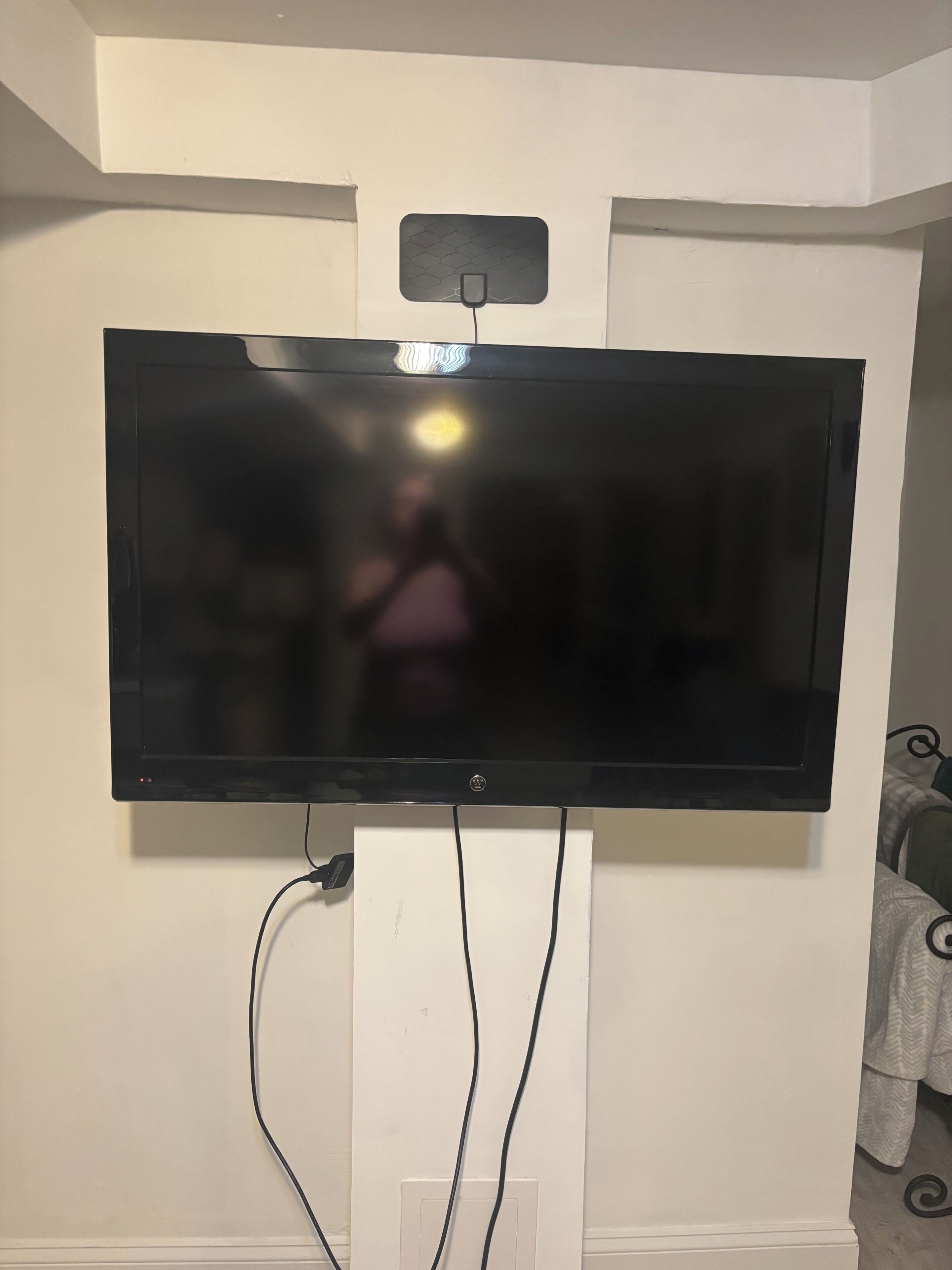 Televisor de pantalla plana montado en una pared blanca, con cables a la vista.
