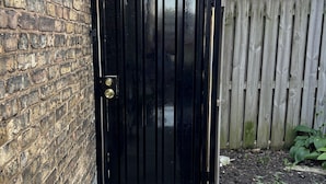 A black metal gate with a keyhole, a brick wall, and a wooden fence. -  3-bedroom apt .on North Side! Great location between downtown and the airport. (Chicago)
