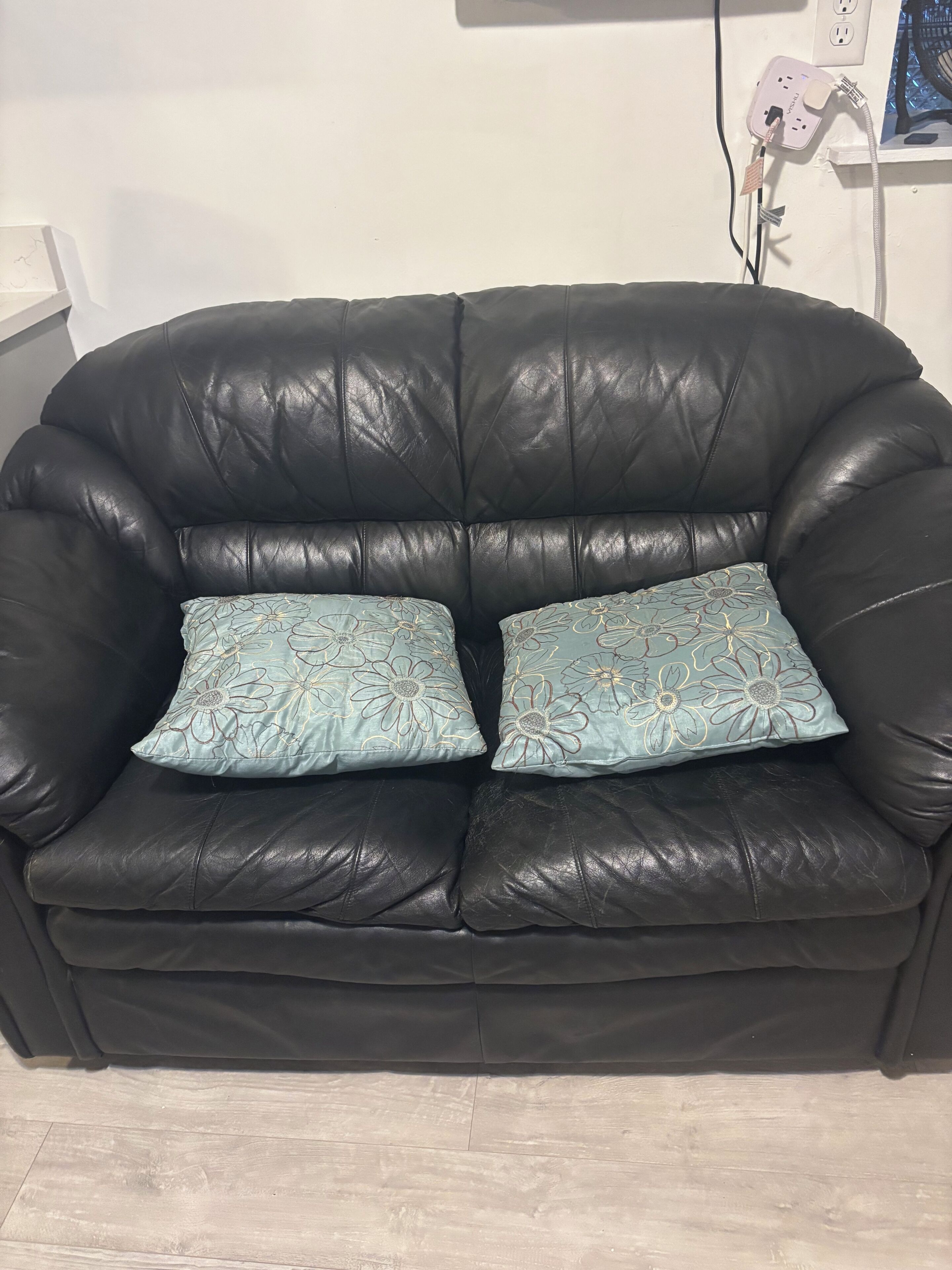 A black leather sofa with floral-patterned cushions.