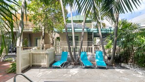 A pool area with lounge chairs, a white fence, and a building with balconies. - Poolside Hide-Away @ Palm Gardens offered by Rent Key West Vacations (Key West)