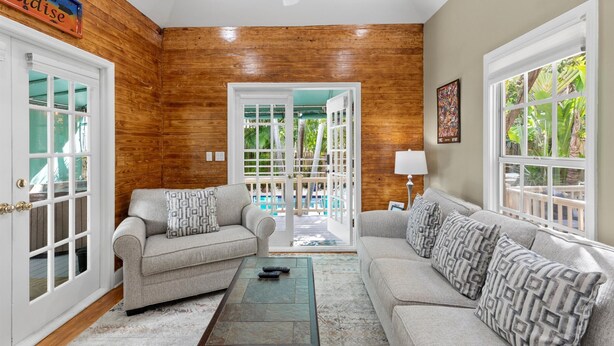 A living room with two sofas, a coffee table, and a view of a pool through glass doors. - Poolside Hide-Away @ Palm Gardens offered by Rent Key West Vacations (Key West)