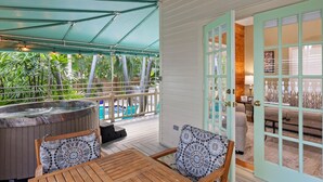A covered outdoor area with a hot tub, wooden furniture, and a view of a pool and greenery. - Poolside Hide-Away @ Palm Gardens offered by Rent Key West Vacations (Key West)