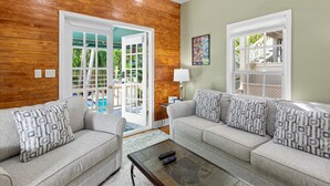 A living room with two grey sofas, patterned cushions, a coffee table, and a wooden wall. - Poolside Hide-Away @ Palm Gardens offered by Rent Key West Vacations (Key West)