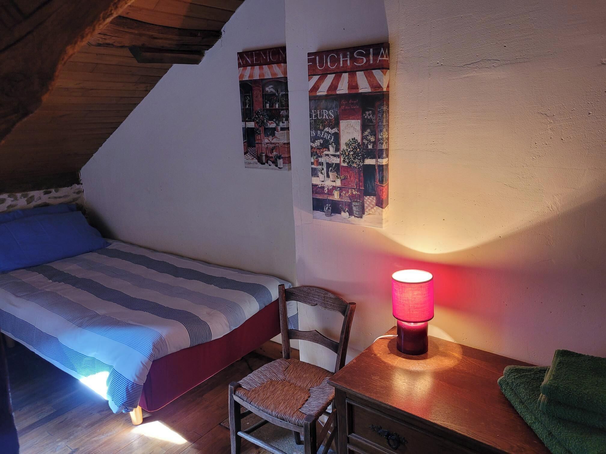 A bedroom with a bed, a chair, a table with a lamp, and two wall decorations.