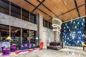 A modern lobby with a high ceiling, large windows, a central seating area with sofas and chairs, a decorative chandelier, and a wall with reflective panels. - Hampton by Hilton Xining Jiaboyuan (Xining)