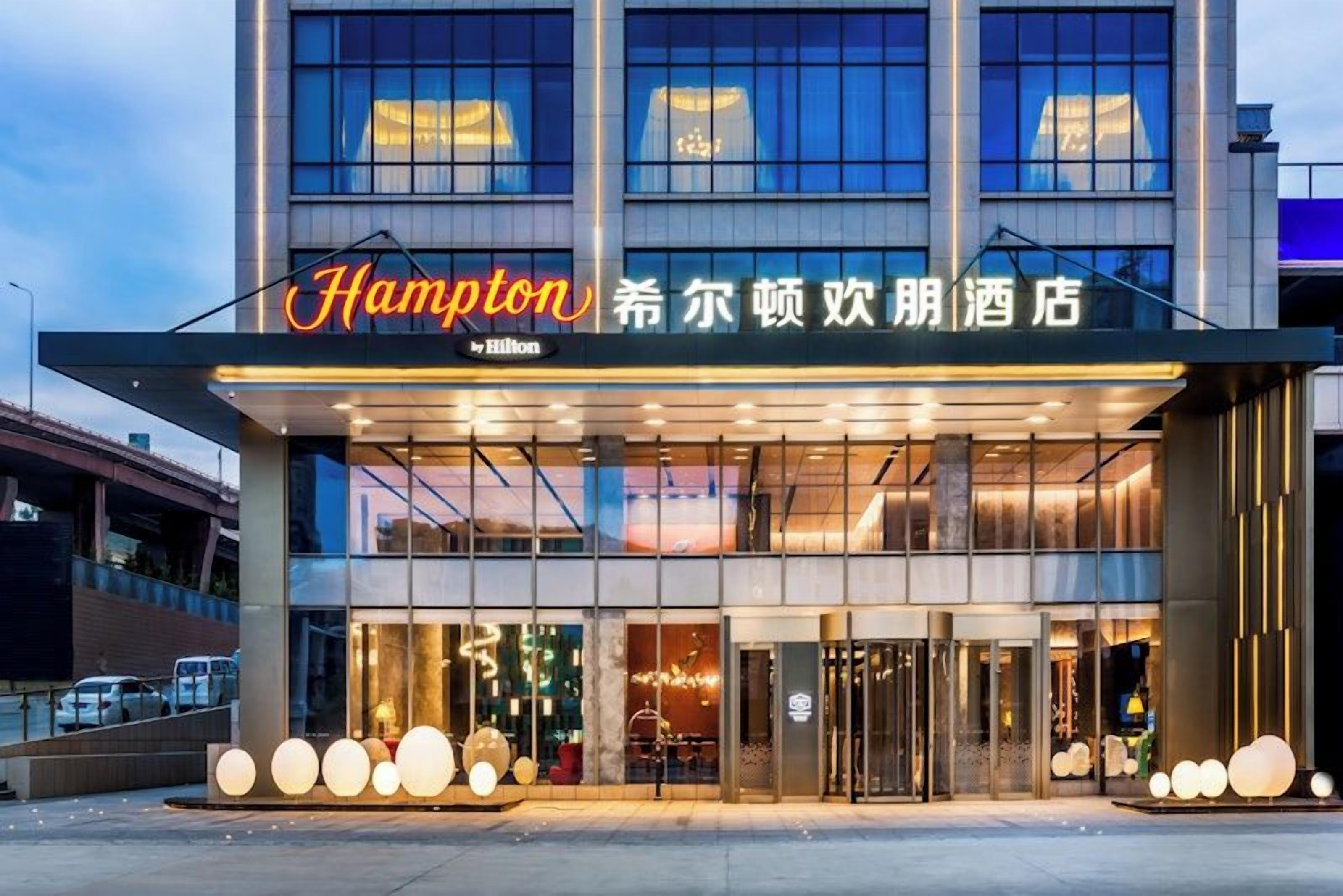 Een Hampton hotel met een moderne gevel, grote glasramen en een opvallende ingang.
