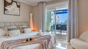 Een moderne hotelkamer met een groot bed, een balkon met een tafel en stoelen, en uitzicht op de zee.
