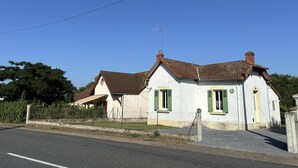 Un bâtiment blanc à deux étages, doté de volets verts et d’un toit recouvert de tuiles brunes.
