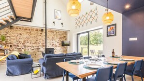 A modern living space with a stone wall, a wooden staircase, a dining area with a table and chairs, and a cozy seating area with a sofa and cushions.