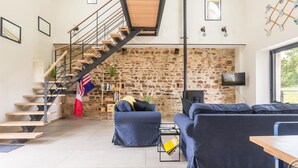 A modern living room with a stone wall, a wooden staircase, a blue sofa, and a television.