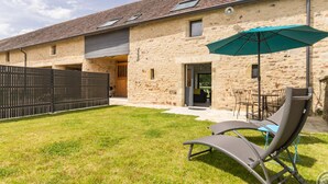 A stone building with a tiled roof, a fenced yard, and outdoor seating with a green umbrella.