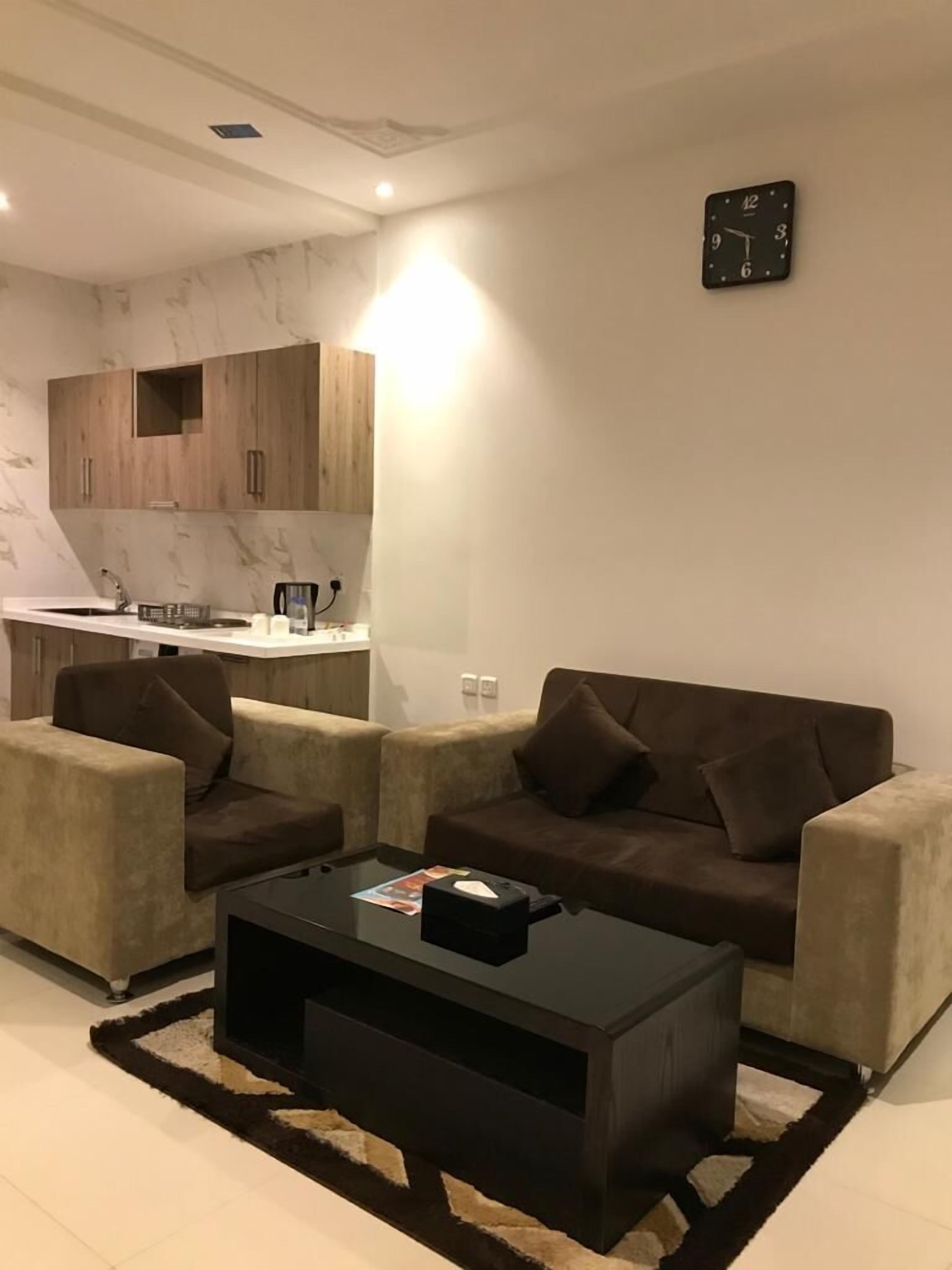 Ein modernes Wohnzimmer mit einem dunklen Couchtisch, zwei braunen Sofas und einem Küchenbereich im Hintergrund.