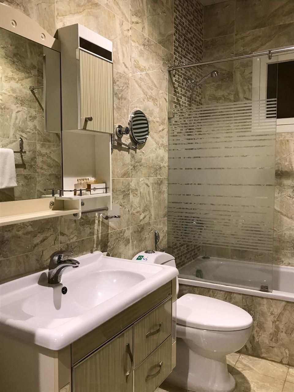 A modern bathroom with a marble sink, a toilet, and a glass-enclosed shower.