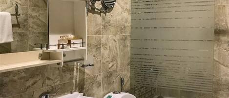 A modern bathroom with a marble sink, a toilet, and a glass-enclosed shower.