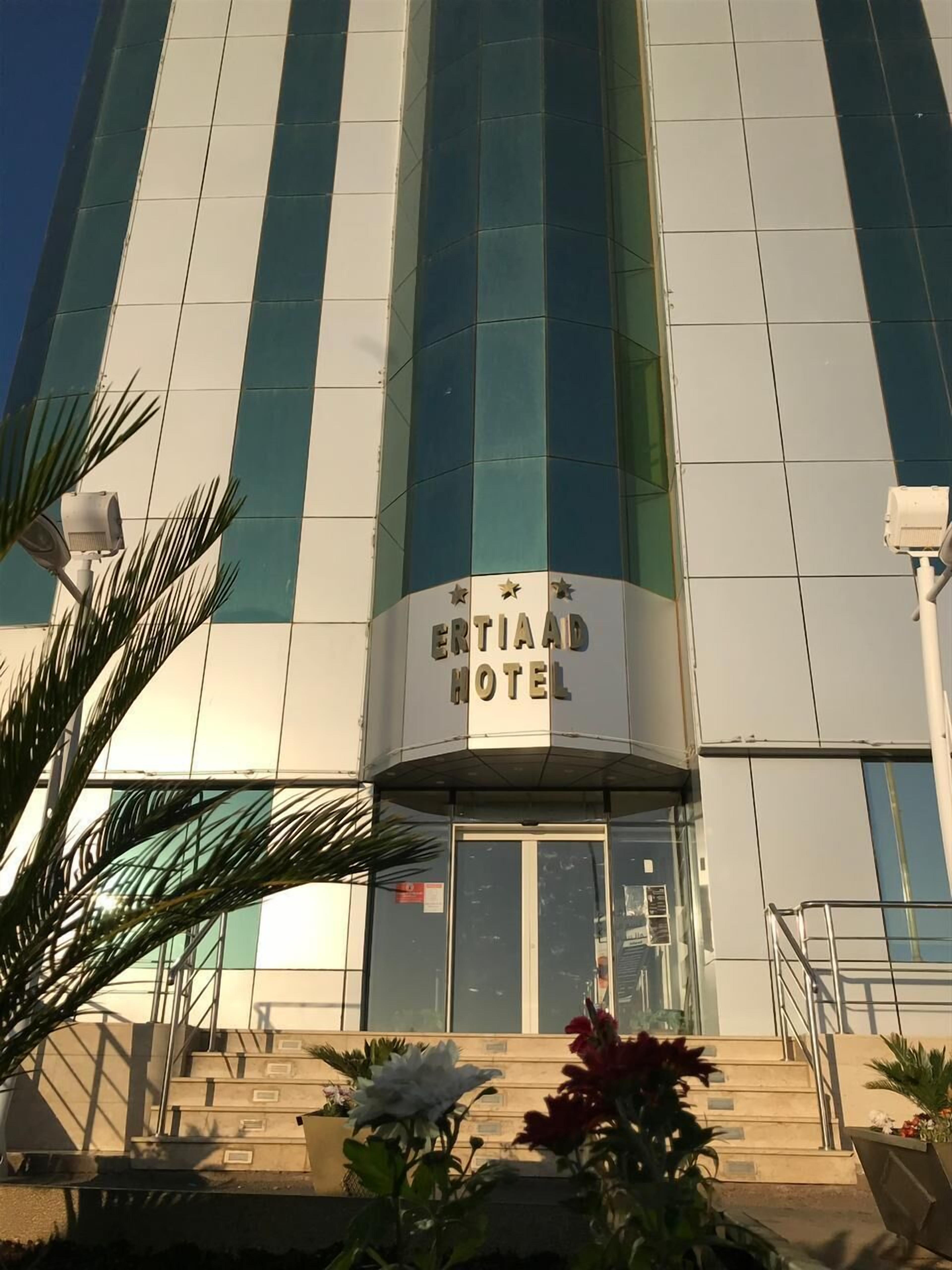 The exterior of the ERTIAAD HOTEL with a modern design, featuring large glass windows and a prominent entrance with a sign.