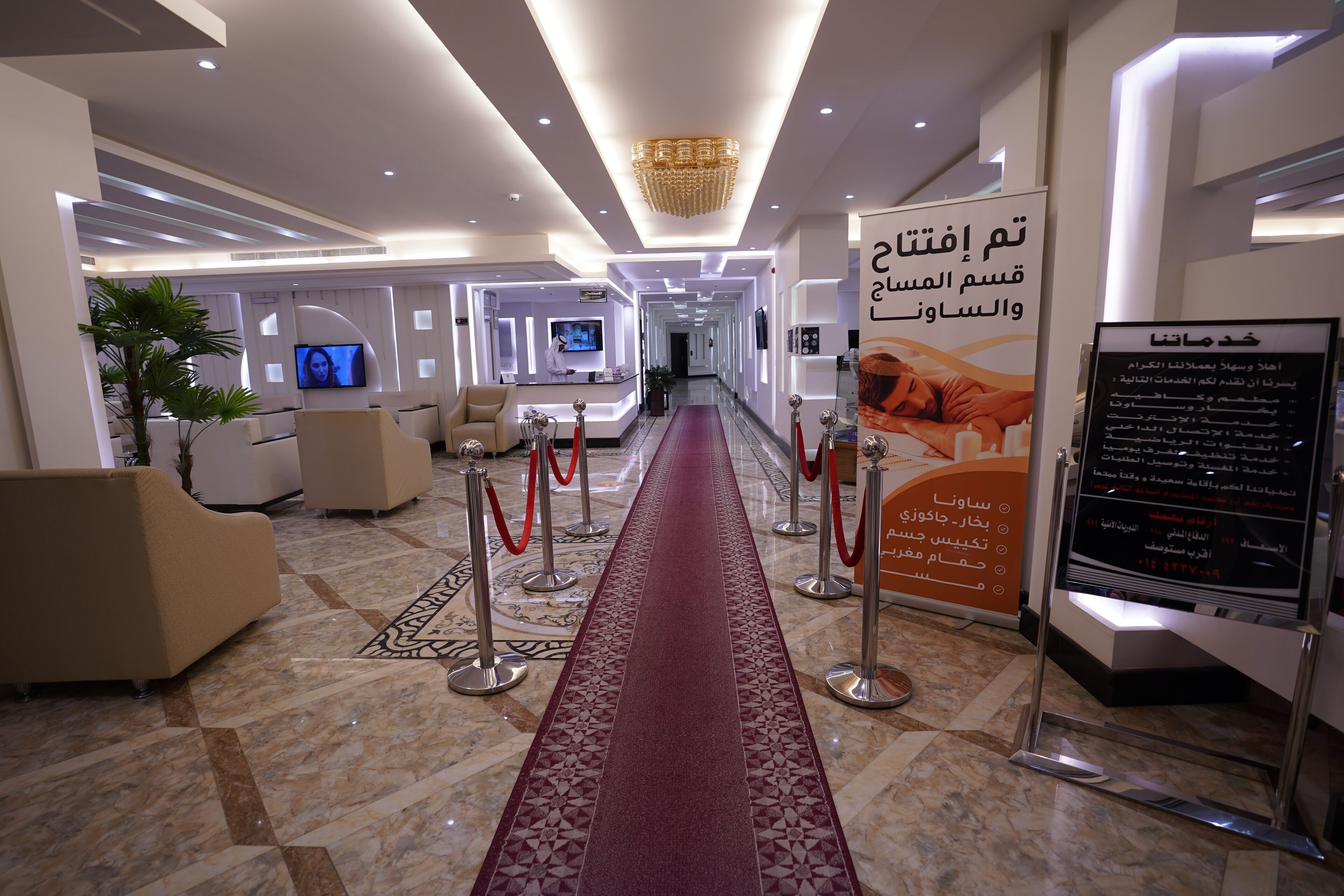A hotel lobby with a red carpet, seating area, reception desk, and a large informational sign.