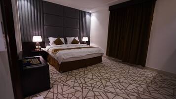 A hotel room with a large bed, dark headboard, patterned carpet, and a nightstand with a lamp.