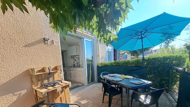 Una veranda esterna con tavolo e sedie, un barbecue e un ombrello blu che offre ombra.