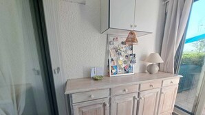 Un armadietto in legno chiaro con cassetti, un tavolino con una lampada e una bacheca con vari appunti e fotografie.