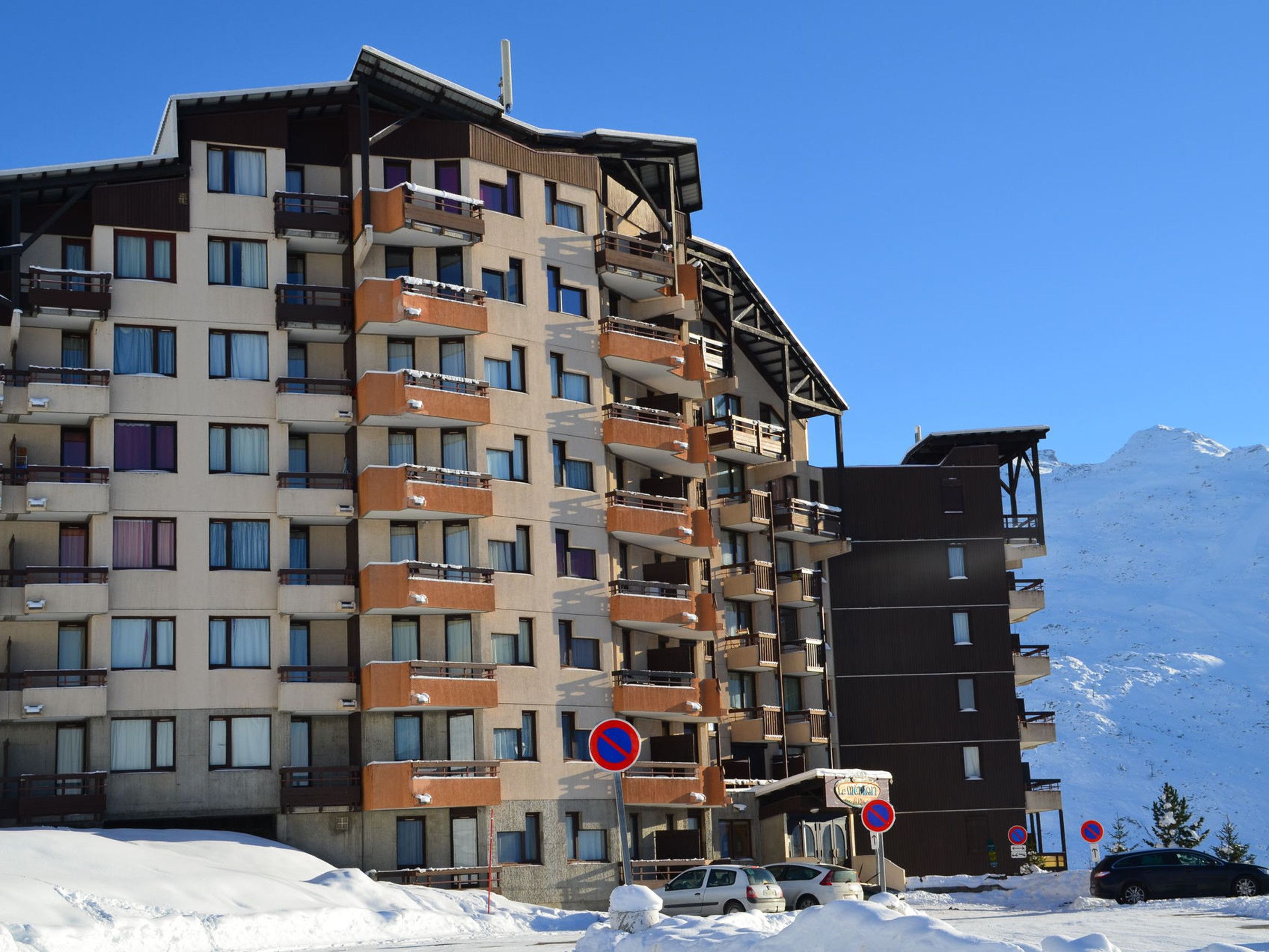 A multi-story hotel with balconies, a ski slope in the background, and a no parking sign.