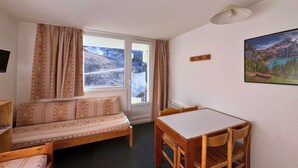 Une pièce chaleureuse avec un canapé, une table à manger et des chaises. Il y a une fenêtre avec des rideaux, un tableau accroché au mur et un luminaire au plafond.