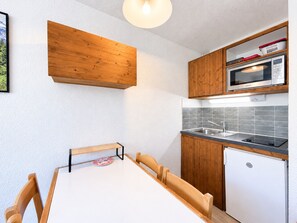 Una cocina compacta con armarios de madera, microondas, pileta y un refrigerador pequeño.
