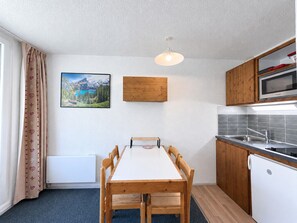 Cocina compacta con mesa de comedor, armarios de madera, microondas y refrigerador.