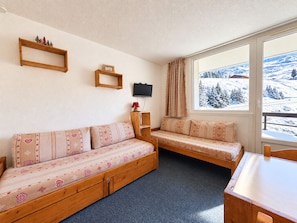 Una habitación acogedora con sofá, una mesita y televisión montada en la pared, y ventana con vistas a un paisaje nevado.
