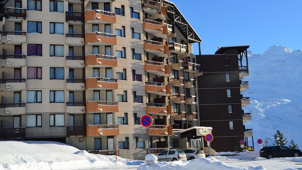 Un hôtel à plusieurs étages doté de balcons, avec une piste de ski en arrière-plan et un panneau indiquant qu’il est interdit de se garer.