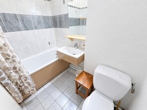 Un baño con bañera, lavamanos, inodoro y un taburete de madera.