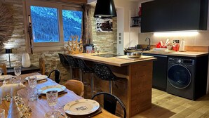 A modern kitchen with a central island, a built-in washing machine, and a dining area with a wooden table set for four.