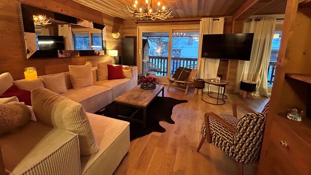 A cozy log cabin interior with a sofa, armchairs, a coffee table, and a TV.