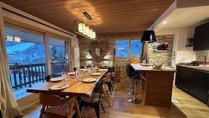 A dining area with a long wooden table, chairs, and a view of snowy mountains through large windows.