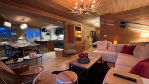 A spacious living area with a wooden ceiling, a dining table set for four, a sofa, and a chandelier.