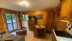 Una habitación acogedora de estilo cabaña, con sofá, mesa de comedor para cuatro personas, televisor y muebles de madera.