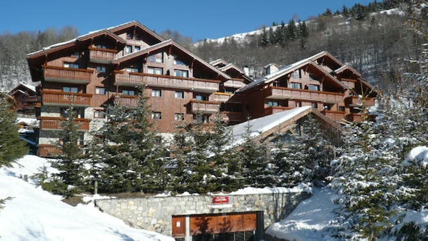Una cabaña de varios pisos con balcones, rodeada de árboles cubiertos de nieve y un muro de piedra.