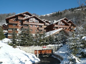 A multi-story lodge with balconies, surrounded by snow-covered trees and a mountain backdrop.