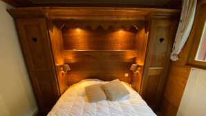Una cama de madera con edredón blanco acolchado, dos lámparas de noche y un cabecero de madera con diseño festoneado.