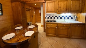 Un interior de madera con una mesa de comedor preparada para cuatro, una zona de cocina con armarios de madera y un salpicadero de azulejos.