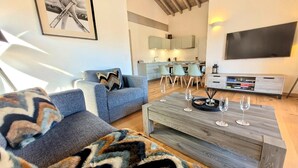 A modern living room with a sofa, coffee table, and a TV. There is a kitchen in the background with a dining area. - Bright apartment 3BR, large balcony (Les Gets)