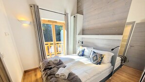 A bedroom with a bed, a wooden headboard, a window with curtains, and a wooden floor. - Bright apartment 3BR, large balcony (Les Gets)