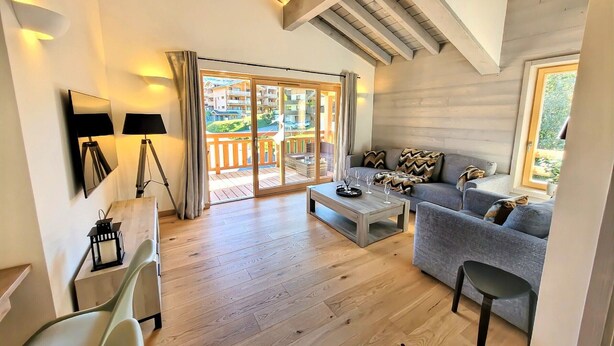A spacious living area with a wooden floor, a sofa, a coffee table, and a balcony with a view of the surrounding buildings. - Bright apartment 3BR, large balcony (Les Gets)