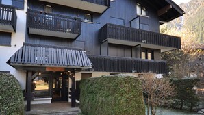A multi-story building with balconies, a covered entrance, and a stone pathway leading to the entrance. - Comfortable renovated studio in green residence in Chamonix (Chamonix-Mont-Blanc)