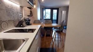 A compact kitchen with a built-in stove, a sink, and a dining area with a table and chairs. - Comfortable renovated studio in green residence in Chamonix (Chamonix-Mont-Blanc)
