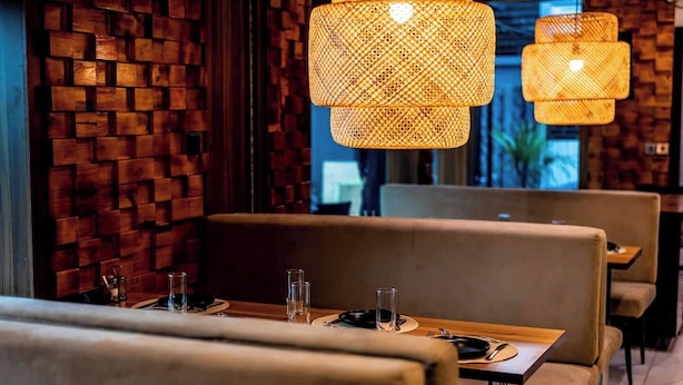 Interior de restaurante con paredes de ladrillo, asientos acolchados y lámparas de ratán colgantes.
