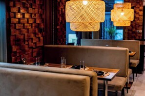 L’intérieur d’un restaurant avec des murs en briques, des banquettes rembourrées et des lampes en rotin suspendues au plafond.