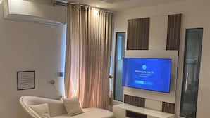 Una sala de estar moderna con un sofá blanco curvo, una mesita de centro redonda y un televisor de pantalla plana montado en la pared.